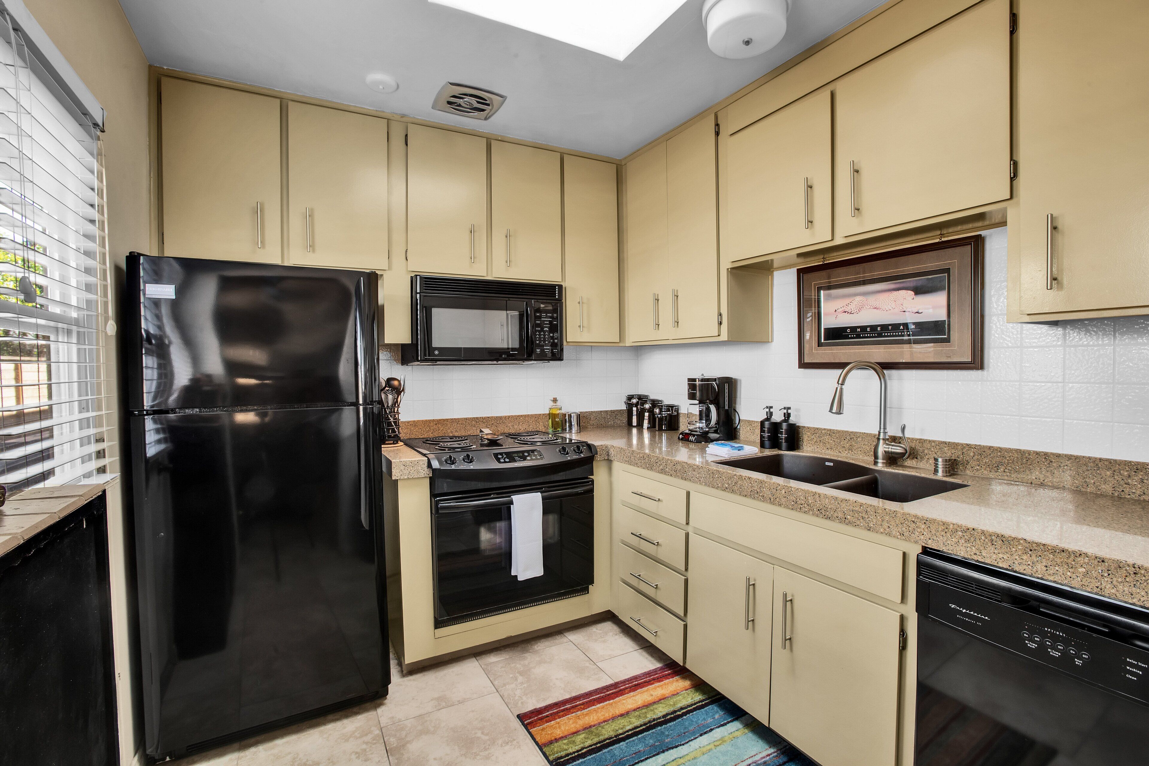 Une cuisine avec des armoires de couleur beige, un réfrigérateur noir, un four à micro-ondes, une cuisinière et un lave-vaisselle.