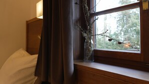 Et værelse med en seng, et natbord, en lampe, et vindue med udsigt til træer og en vase med grene på natbordet.