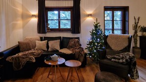En hyggelig stue med sofa, sofabord og juletræ. To vinduer med gardiner, en vægmonteret lampe og en loftventilator.