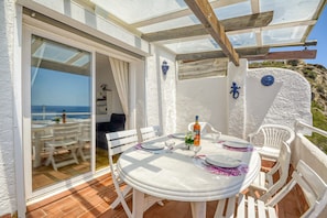 An outdoor patio with a round table, white chairs, and a glass door leading to a terrace. - House in Rosas With Waterfront & Beach Nearby (Roses)