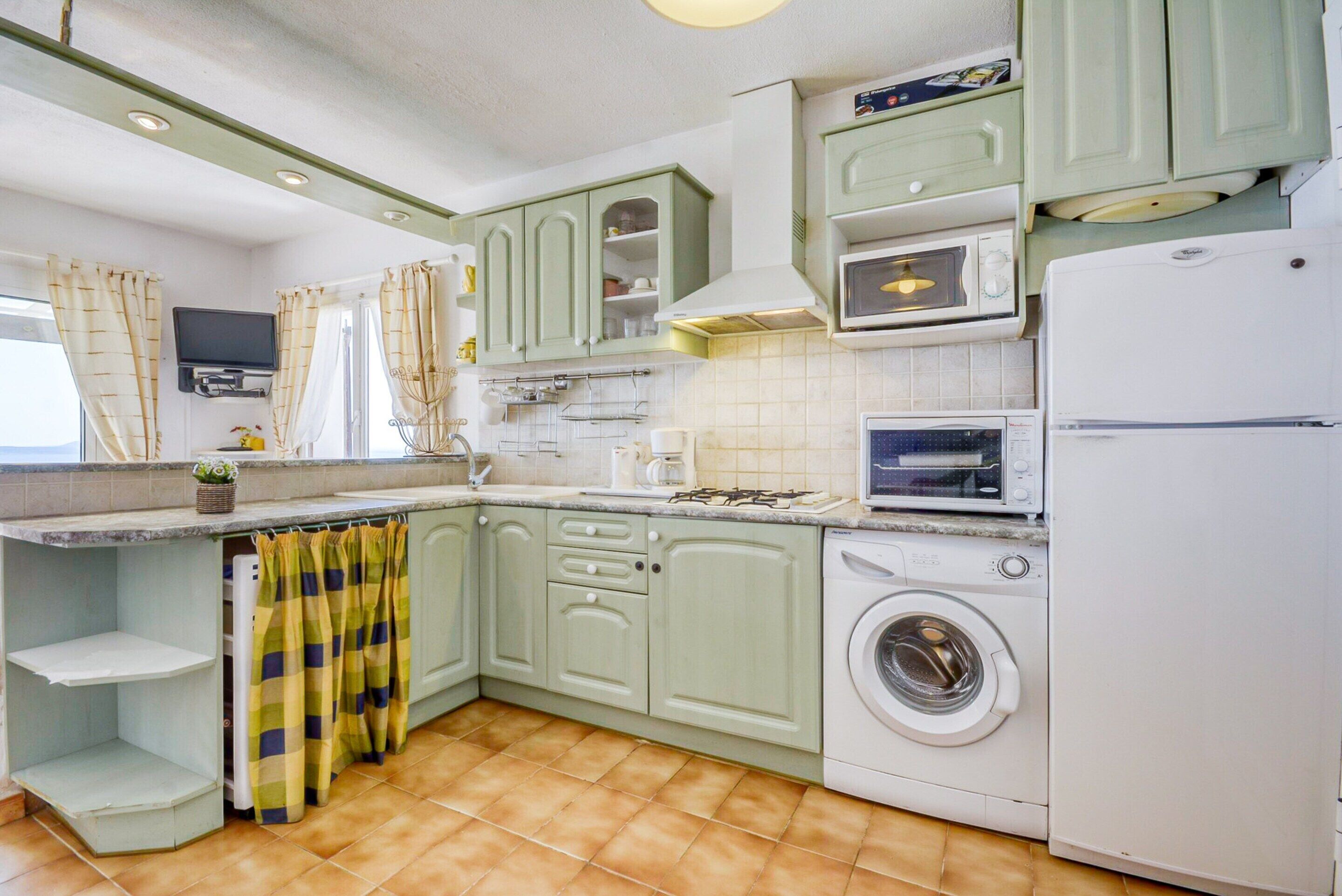 A compact kitchen with green cabinets, a washing machine, a microwave, and a small TV.