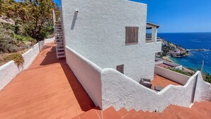 A white building with a red-tiled roof, a staircase, and a view of the sea. - House in Rosas With Waterfront & Beach Nearby (Roses)