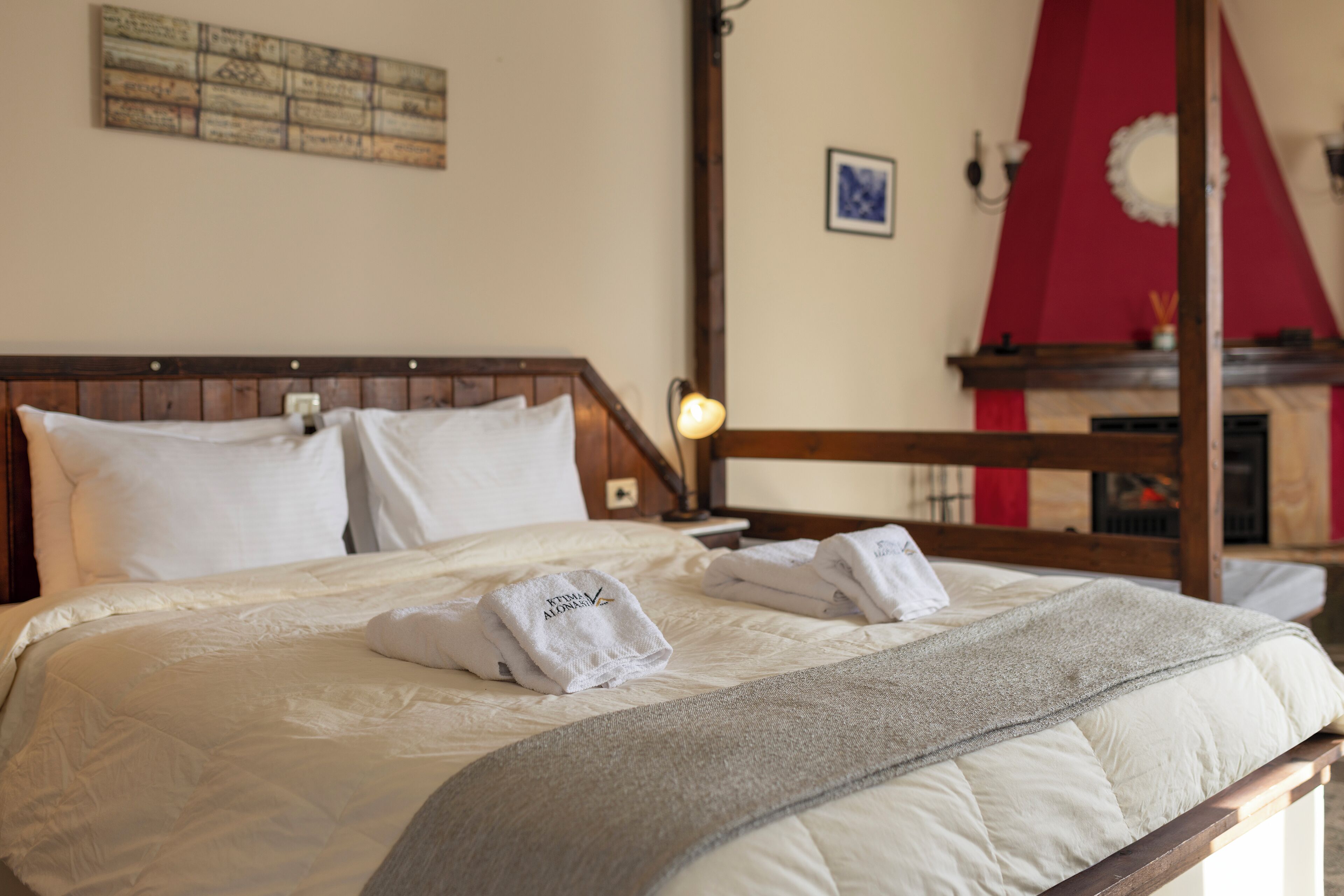 Una cama bien hecha con sábanas blancas y un plaid gris, cabecera de madera y una lámpara fijada a la pared.