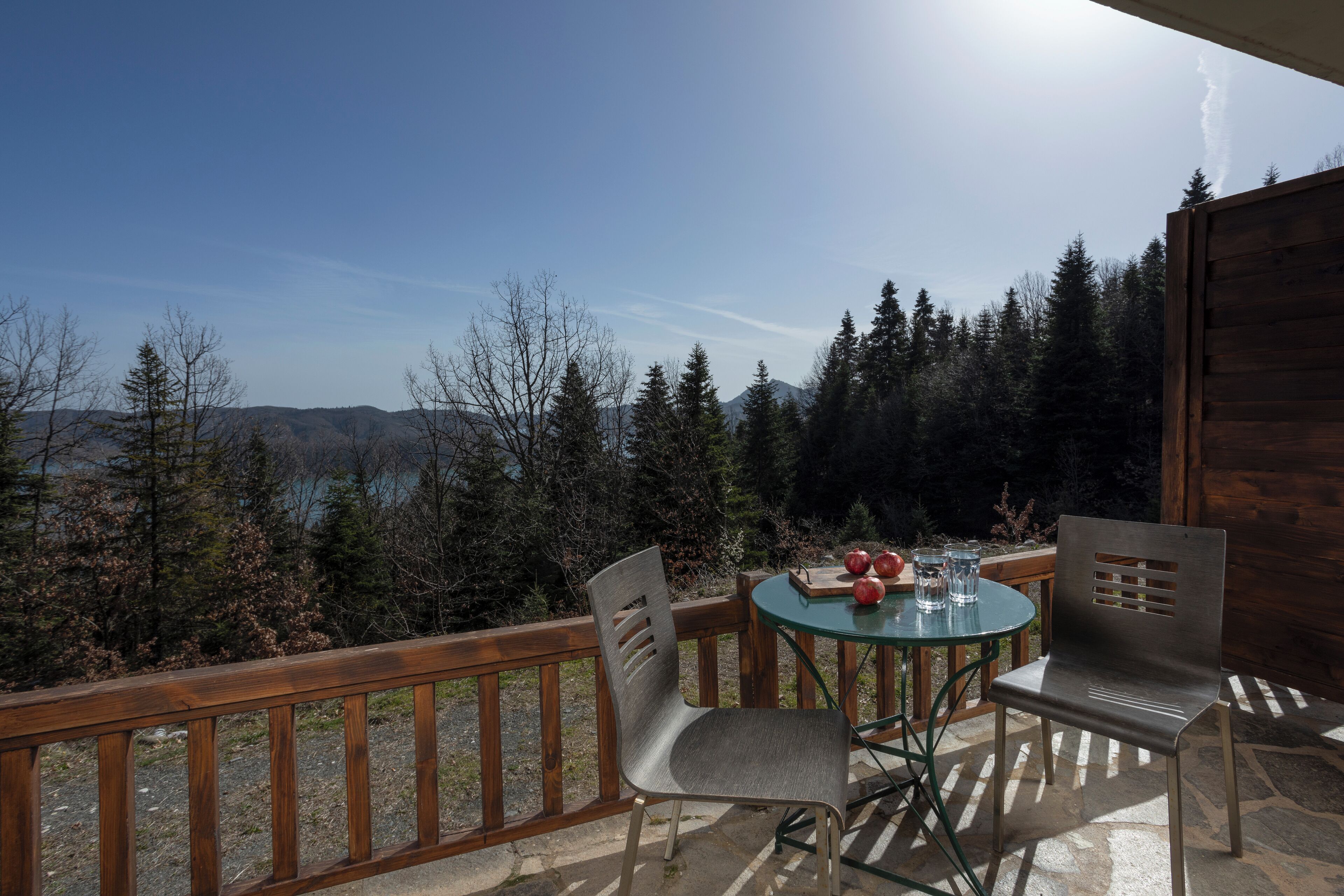 Une terrasse en bois avec une table et des chaises en verre, donnant sur une vallée boisée.