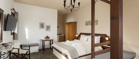 A bedroom with a stone floor, a wooden bed frame, a desk with a chair, a television, and a chandelier.