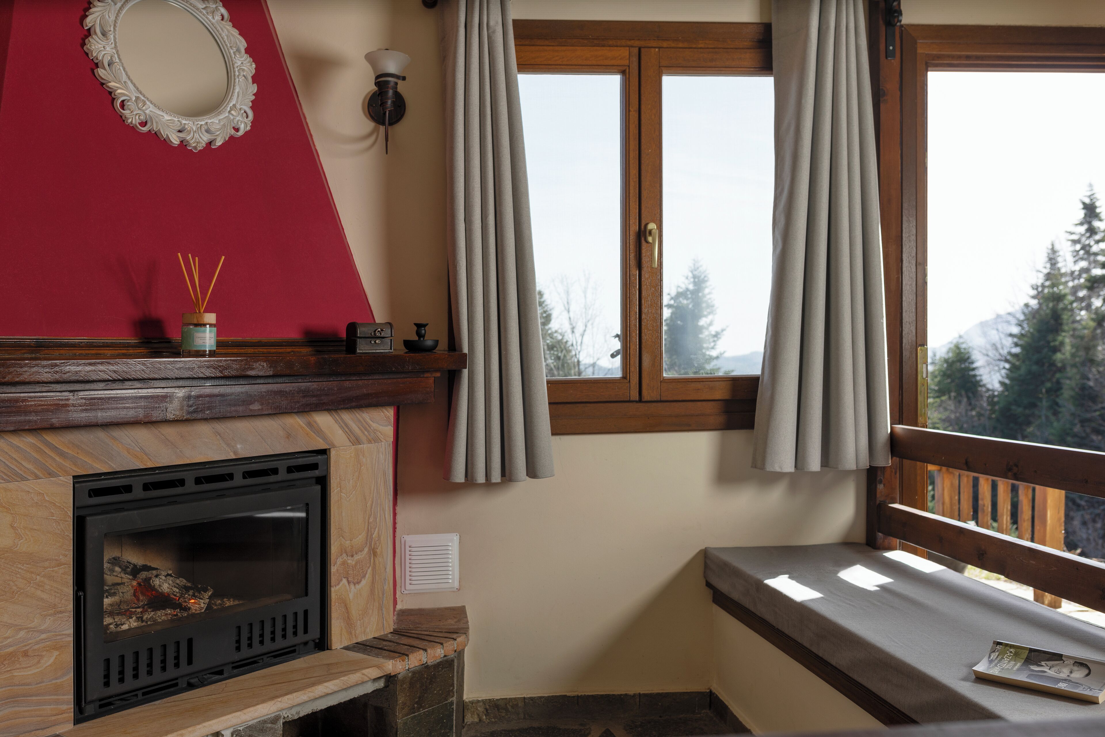 A cozy room with a fireplace, a bench, a window with curtains, and a view of trees.