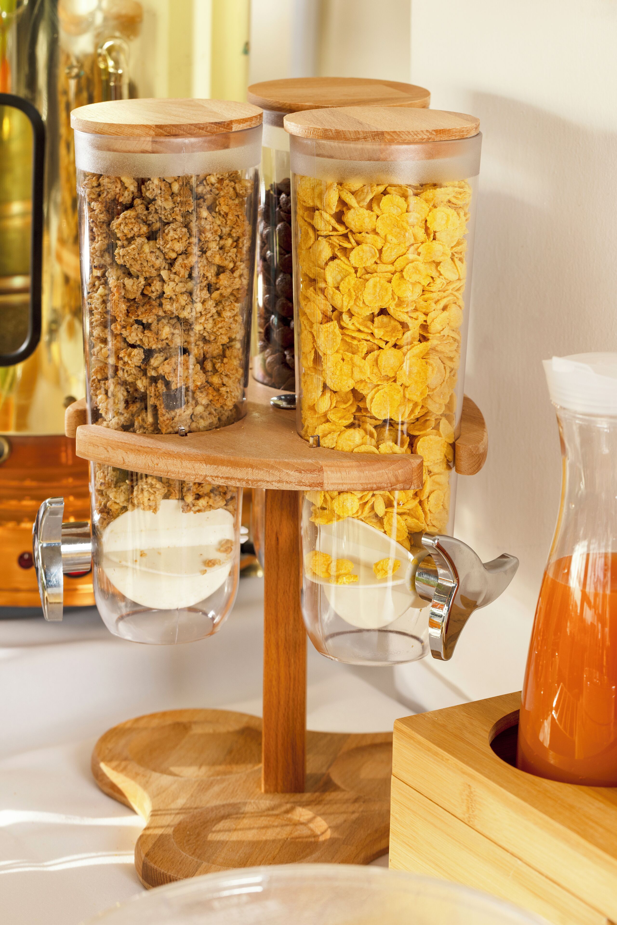 A breakfast bar with three glass containers holding granola, chocolate chips, and cornflakes.