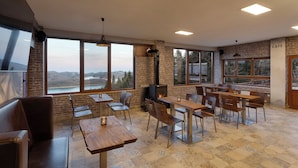 A spacious cafe with large windows offering scenic views, wooden tables and chairs, and a fireplace. - Ktima Alonaki (Lake Plastiras)