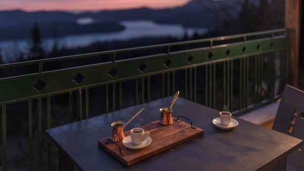 A table with two cups of coffee and a small pot on a wooden tray, set against a scenic mountain view. - Ktima Alonaki (Lake Plastiras)