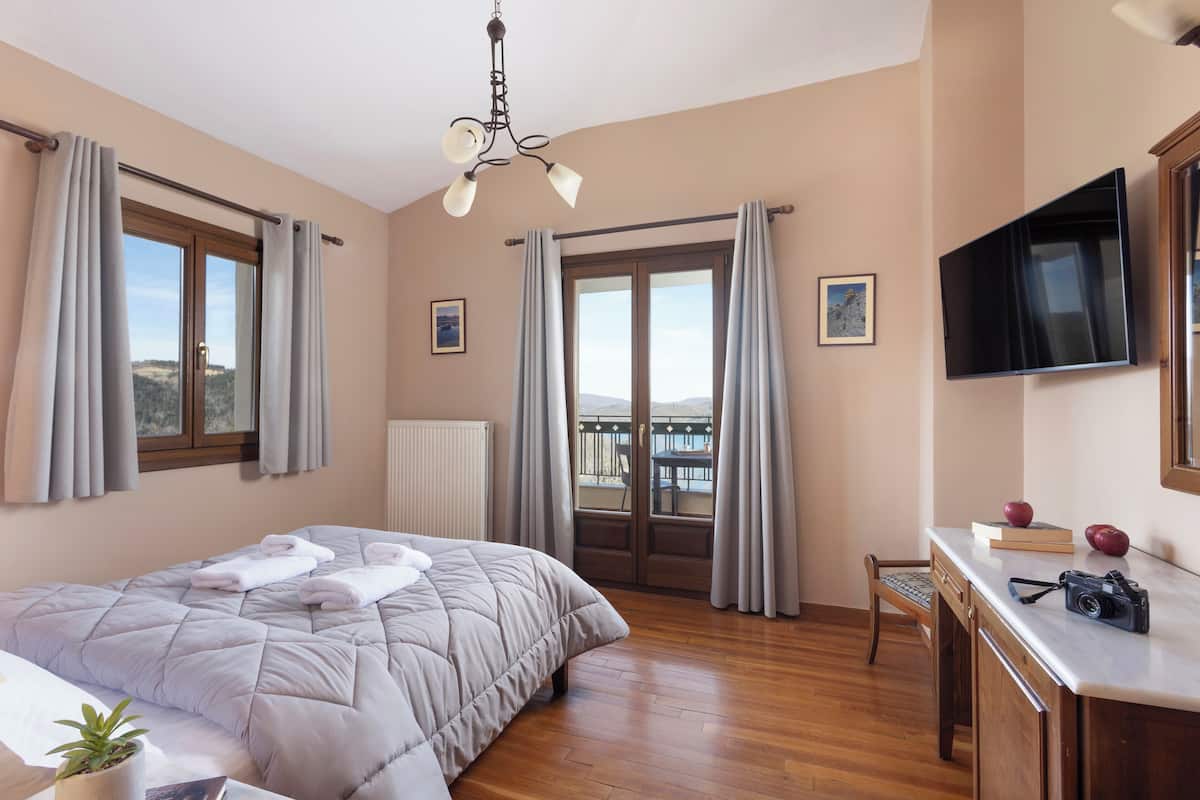Ein Hotelzimmer mit einem Bett, einem Schreibtisch, einem Sessel, einem Fernseher und einem Balkon mit Vorhängen.