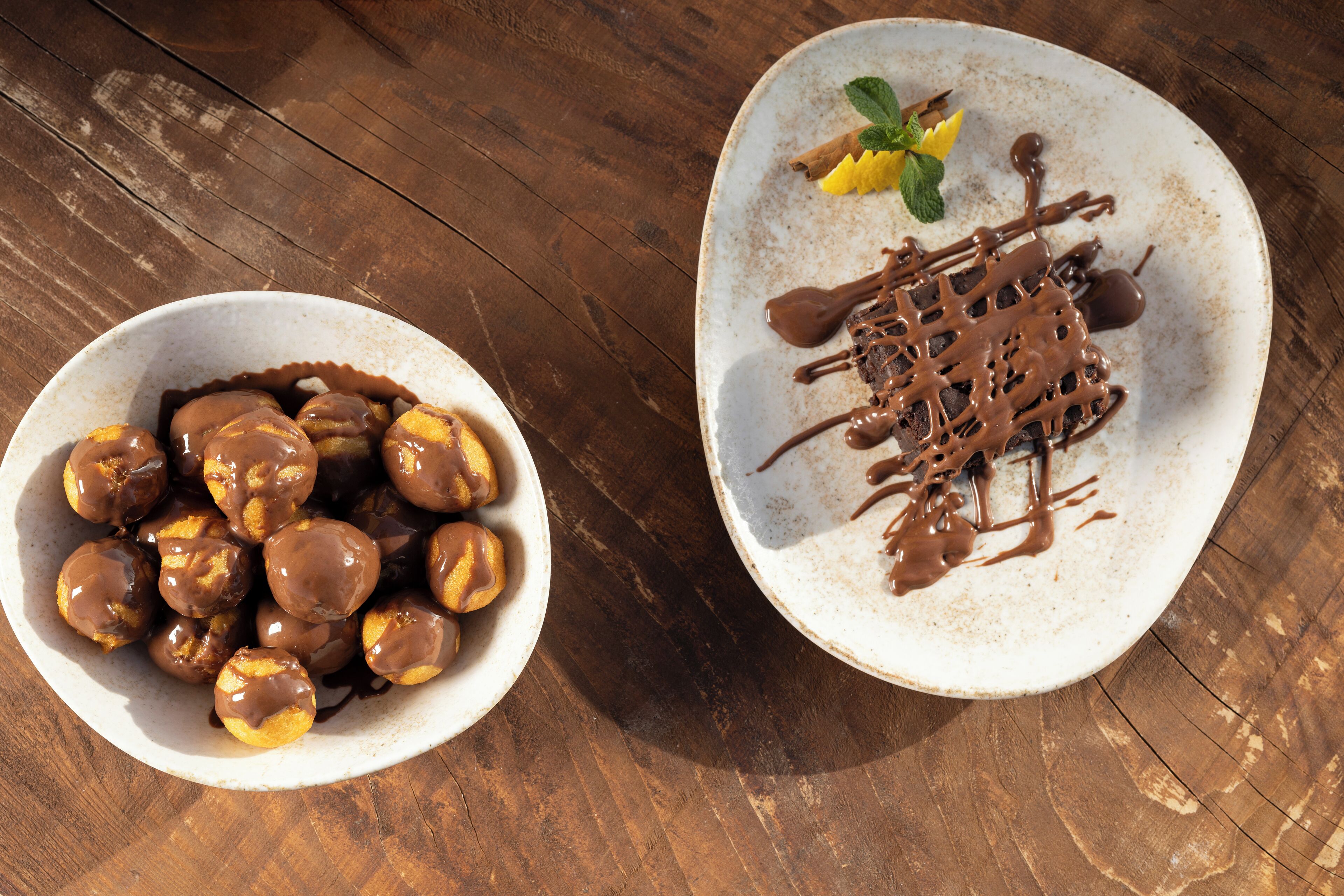 Dos tazones de pasteles bañados en chocolate sobre una mesa de madera.
