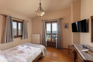 A bedroom with a bed, a desk, a chair, a television, and a balcony with curtains.