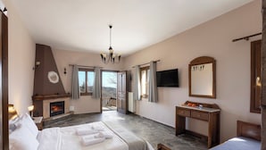 A bedroom with a fireplace, a bed with white linens, a desk, a television, and a view of the outdoors. - Ktima Alonaki (Lake Plastiras)