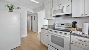 A modern kitchen with white cabinetry, a built-in microwave, oven, and a granite countertop. - Waterfront | Fishing Pier | Walk to Beach (Cocoa Beach)