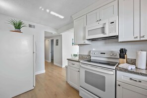 A modern kitchen with white cabinets, a microwave, an oven, and a granite countertop. - Waterfront | Fishing Pier | Walk to Beach (Cocoa Beach)