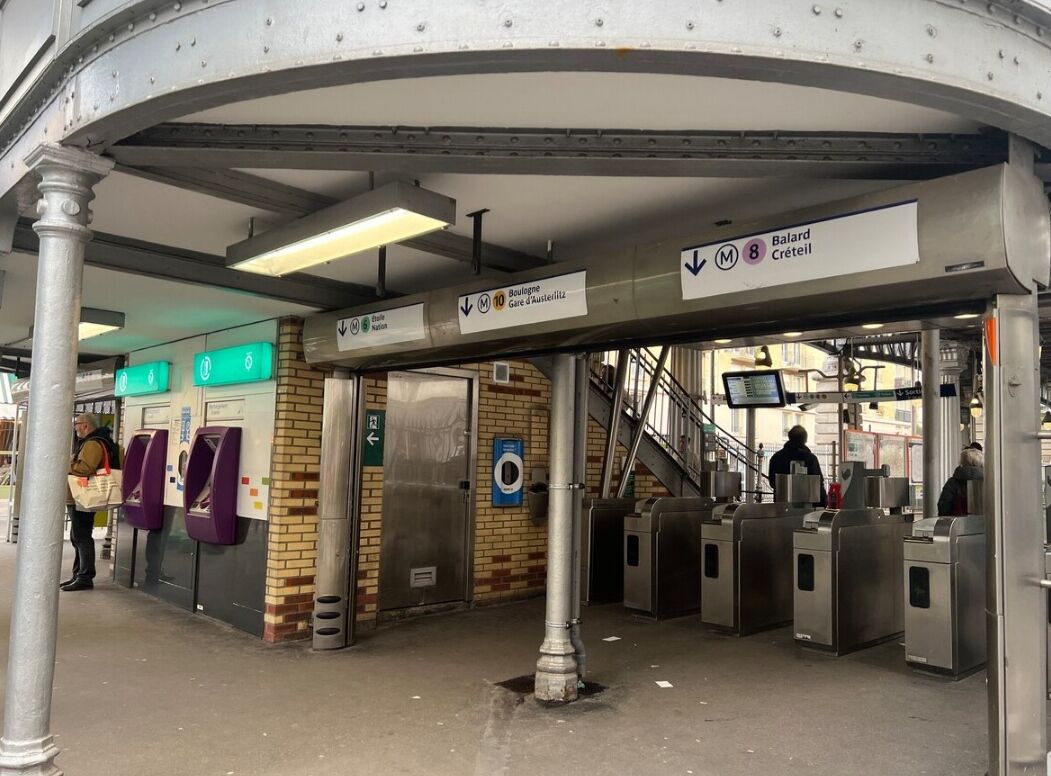 A subway station with turnstiles, a staircase, and directional signs.