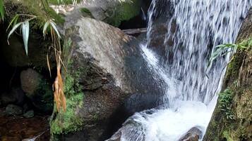 Una persona sentada sobre rocas cerca de una cascada en un entorno natural.