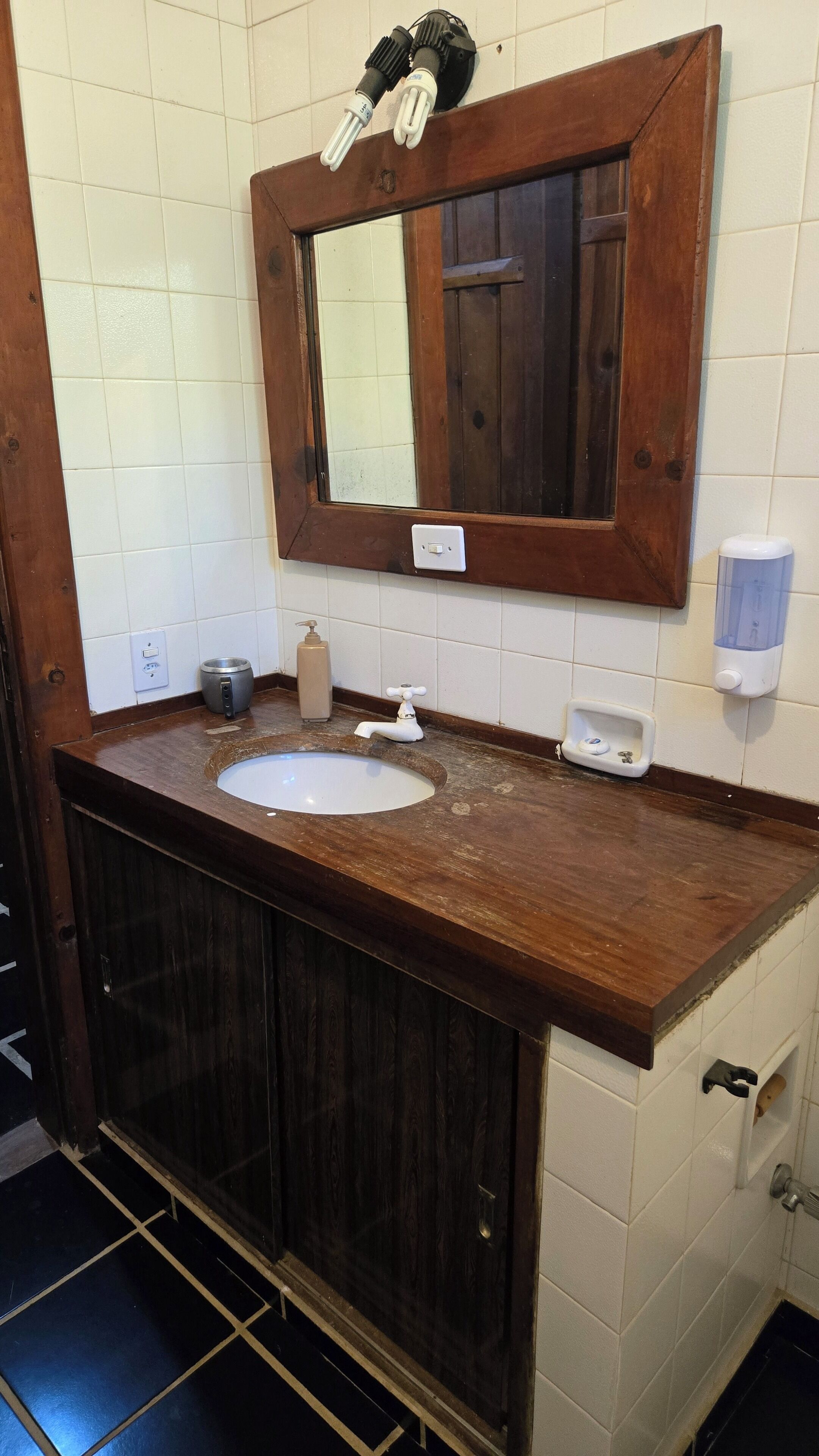 A bathroom with a wooden vanity, a sink, a mirror, and a soap dispenser.