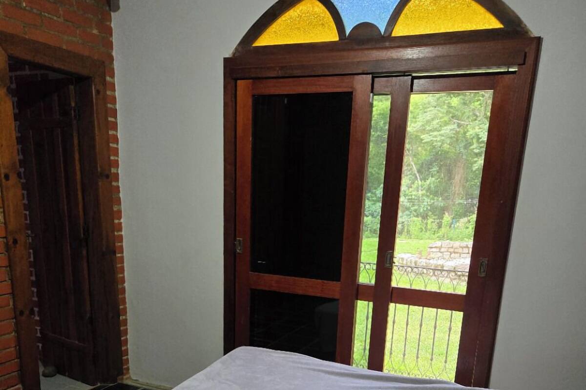 Una habitación con una cama, una puerta de madera con vidrieras y vistas al exterior.