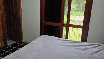 Une chambre avec un lit, une porte en bois ornée de vitraux et une vue sur la verdure à l’extérieur.