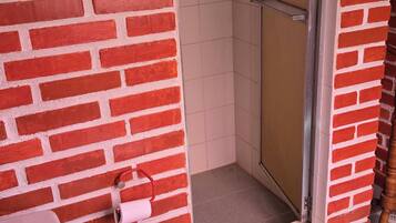 Un baño con inodoro rojo, ducha con puerta de cristal y pared de azulejos blancos.