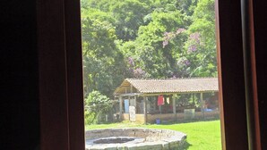 A wooden door with a view of a lush green landscape, a small building, and a stone fountain. - Maple Leaf Ecovillage Camping & Reserve (Resende)