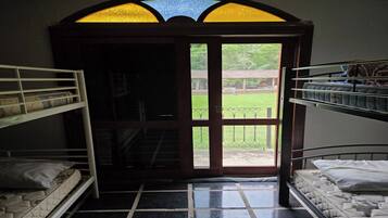 A room with bunk beds, a large arched window, and a view of a green landscape.