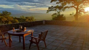 A stone patio with a round table and chairs, overlooking a scenic landscape with mountains and a tree. - Maple Leaf Ecovillage Camping & Reserve (Resende)