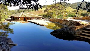 A rustic building with a tiled roof near a calm pool, surrounded by natural scenery and stone steps. - Maple Leaf Ecovillage Camping & Reserve (Resende)