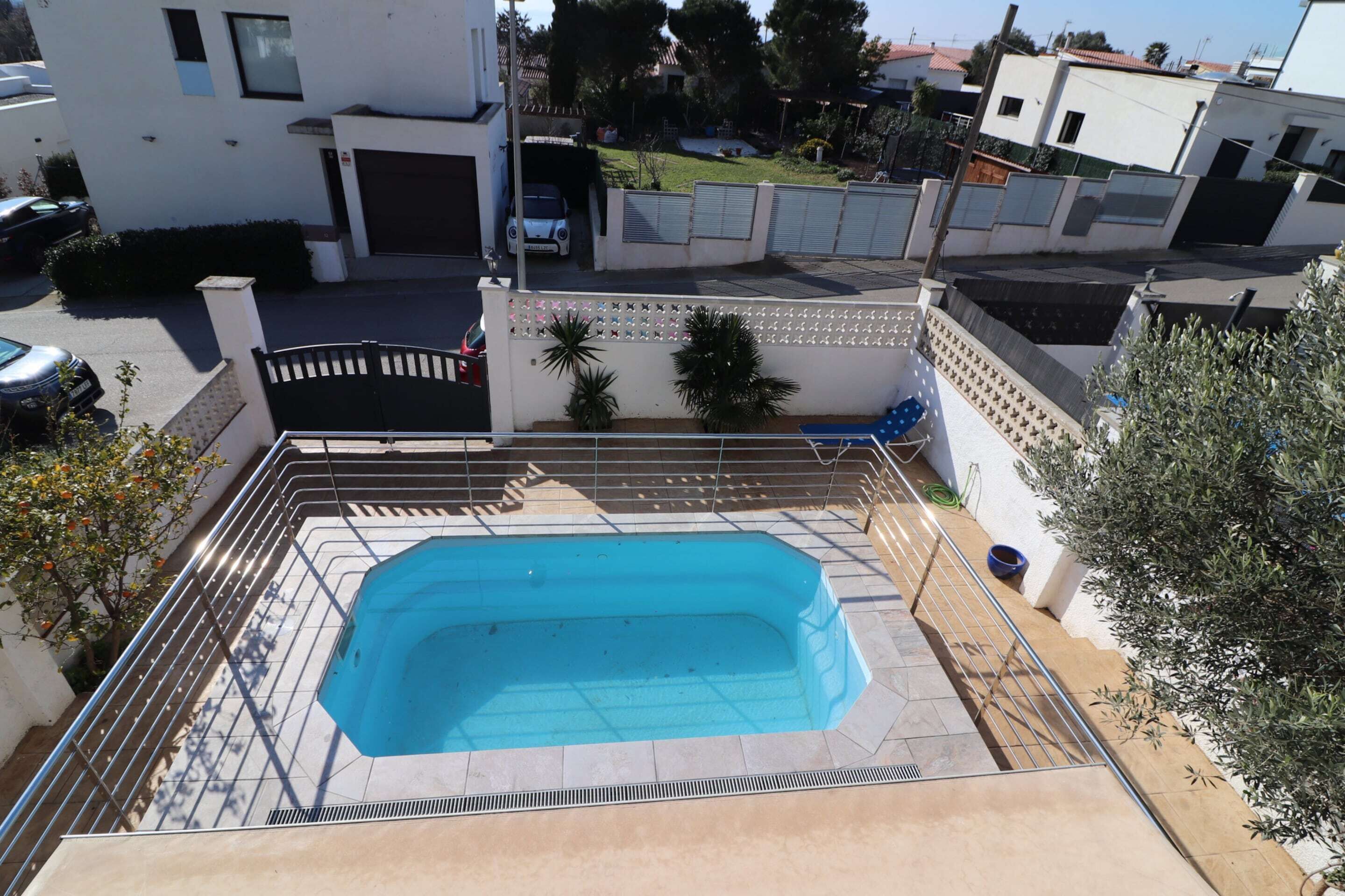 Una piscina rettangolare con una recinzione metallica di sicurezza, circondata da un solarium piastrellato.