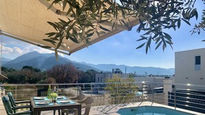 A poolside area with a table and chairs, a covered seating area, and a view of mountains in the background. - Beautiful Apartment With View (Roses)