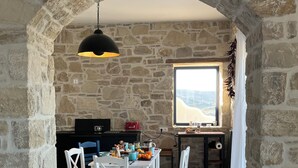 A stone-walled dining area with a table set for two, a hanging light fixture, and a view through a window. - Quiet house in southern Crete, picturesque sea and mountain views, beach within walking distance (Pitsidia)