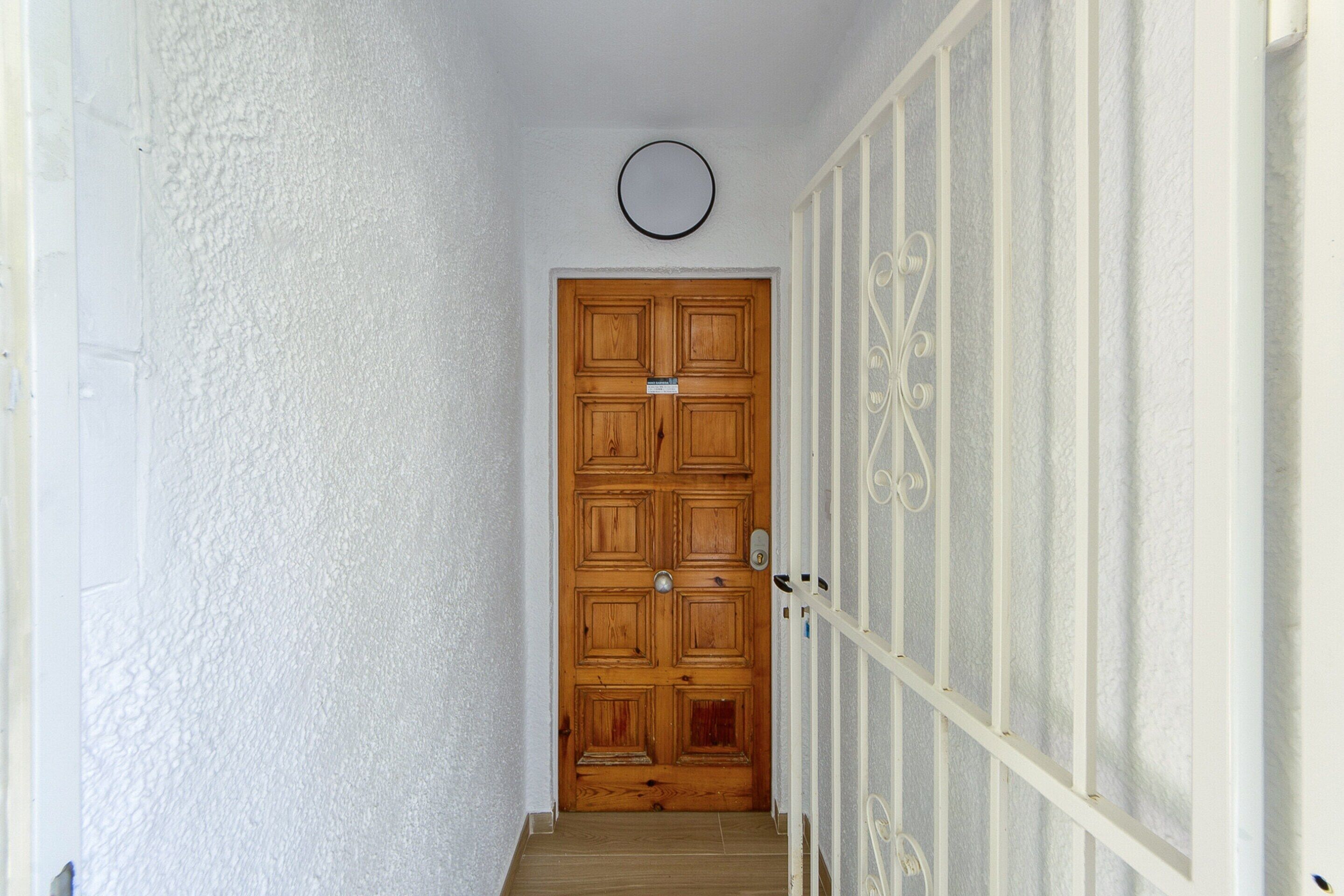 A hallway with a wooden door, white walls, and a white railing.