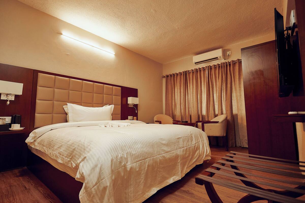 A hotel room with a large bed, a desk, a chair, and a TV.