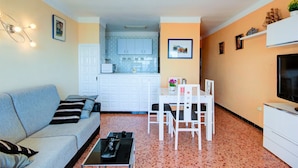 A compact living space with a sofa, dining table, chairs, a TV, and a kitchenette in the background. - Apartment in Roses by the Beach & Marina (Roses)