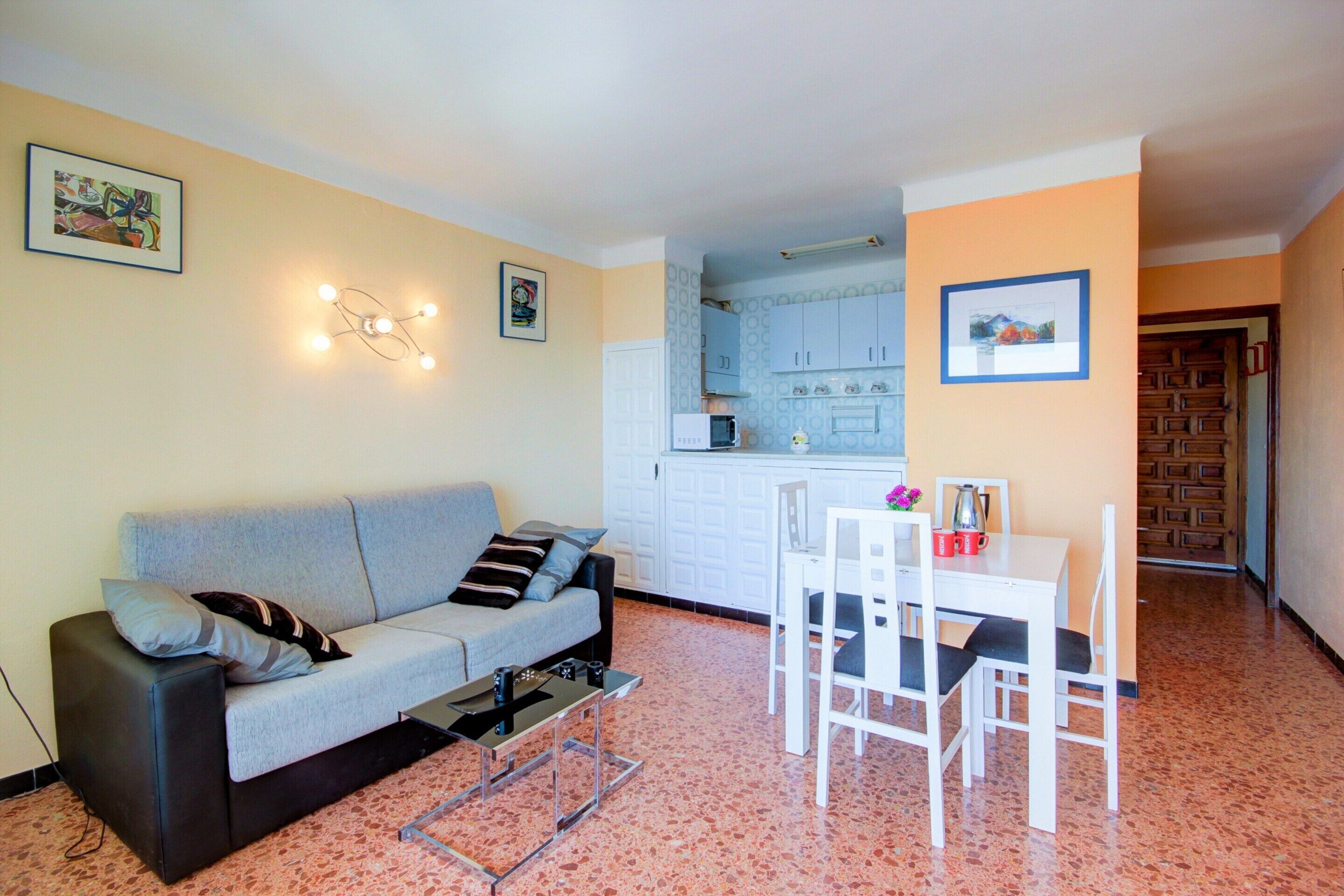 A compact living space with a sofa, a dining table with chairs, a kitchen area with cabinets and a microwave, and a small coffee table.