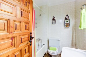 A bathroom with a wooden door, a bathtub, a toilet, and two wall-mounted shelves with decorative items. - Apartment in Roses by the Beach & Marina (Roses)