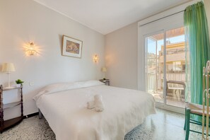 A hotel room with a bed, two wall-mounted lamps, a framed picture, a small table with a plant, and a view of the outside balcony. - Apartment by Roses Beach With Mountain Views (Roses)