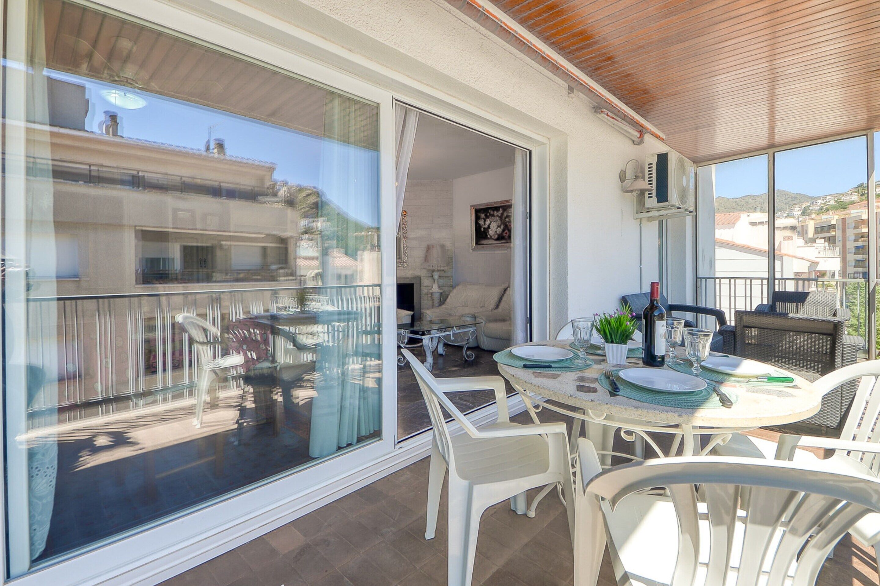 A balcony with a glass door leading to a dining area with white furniture and a table set for two.