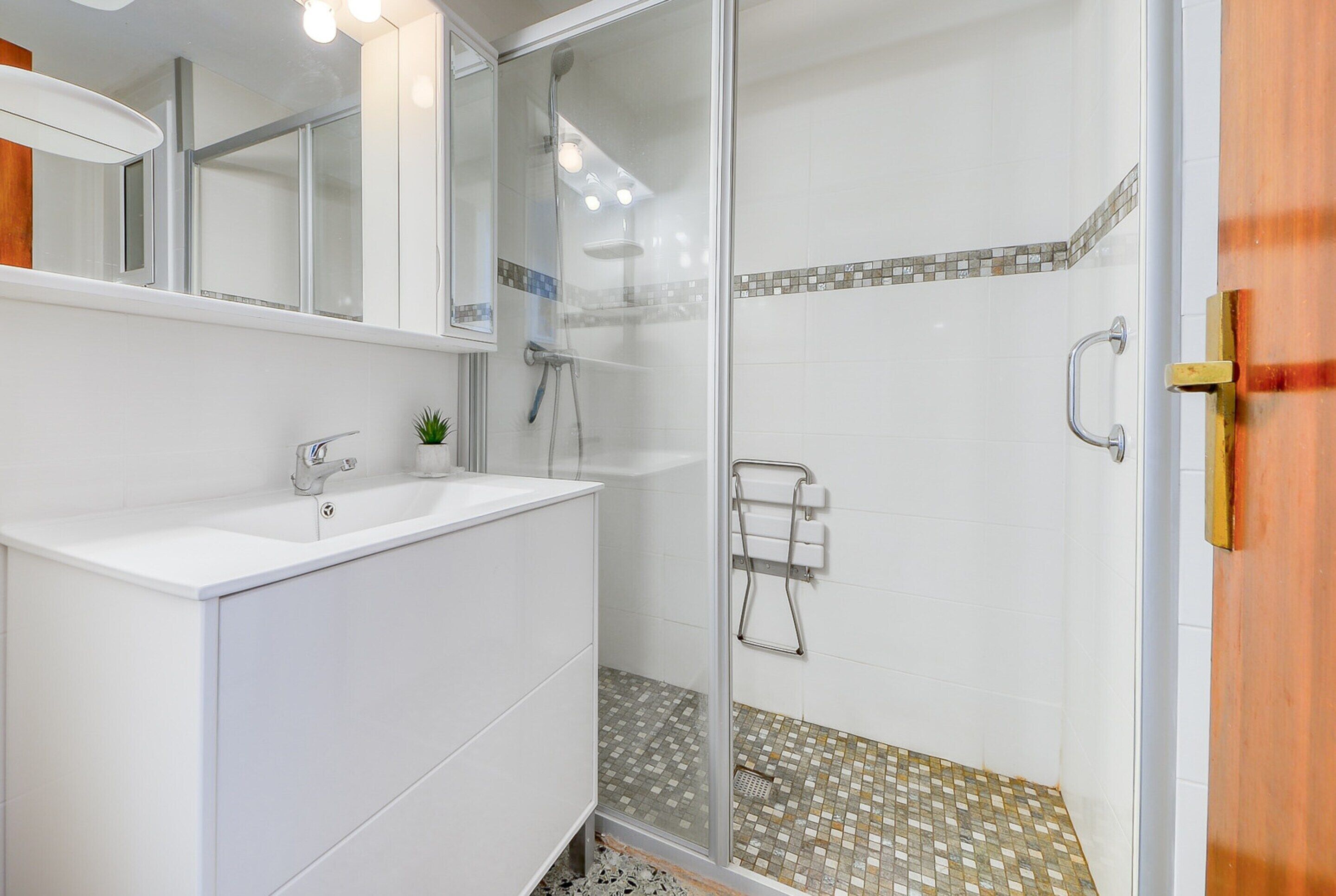 A modern bathroom with a glass shower enclosure, a white sink, and a mirror above it.