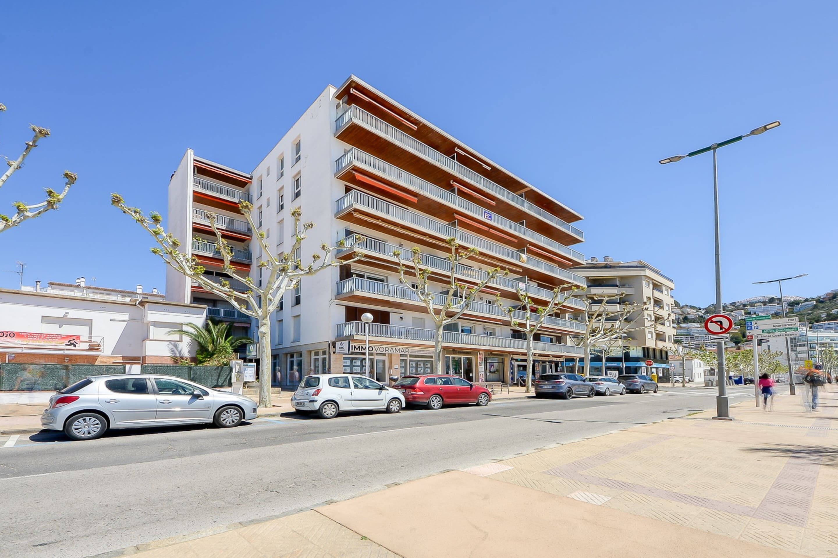 Un edificio a più piani con balconi, una strada con auto parcheggiate e un marciapiede.
