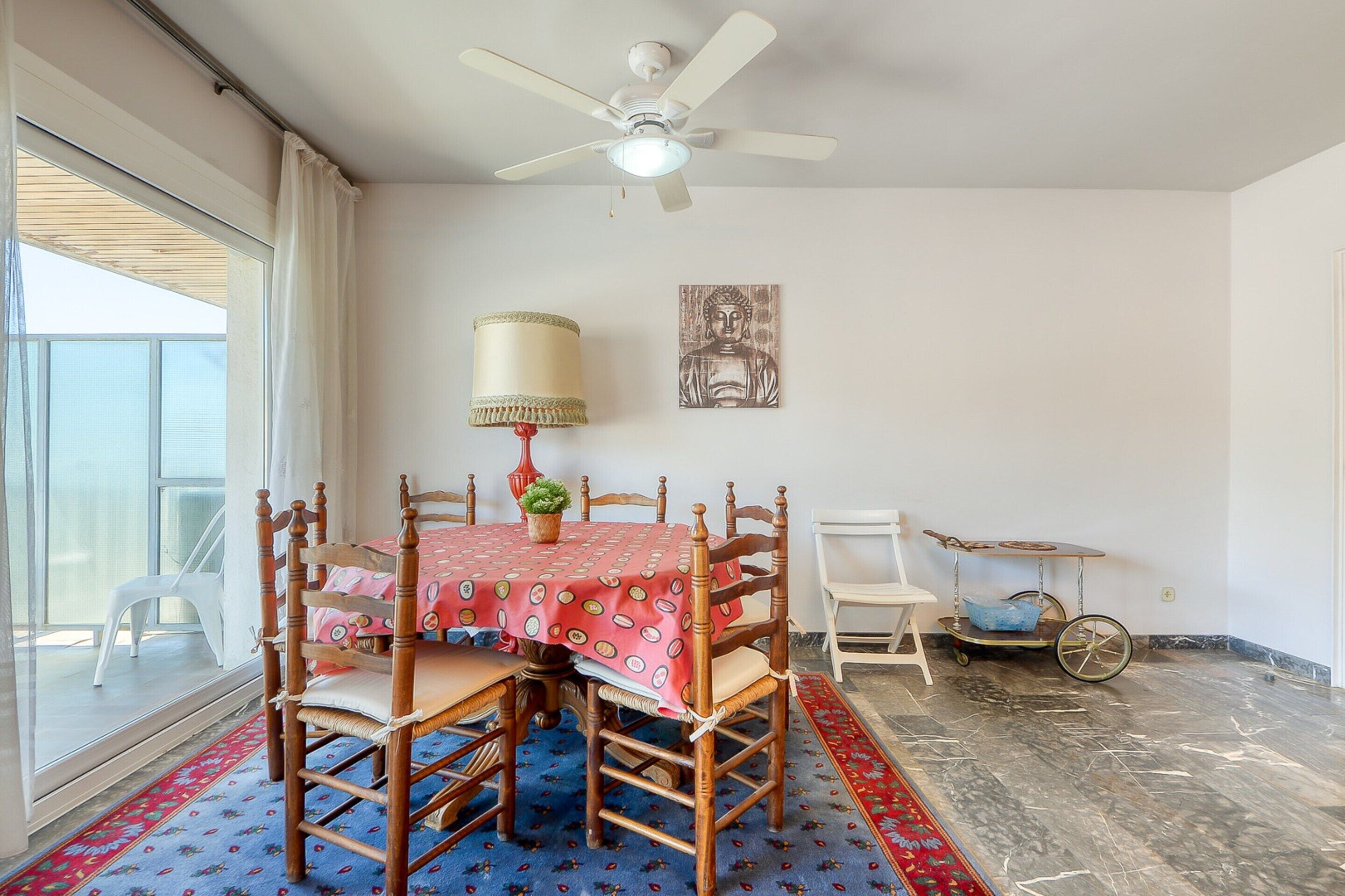 A dining area with a table set for four, a ceiling fan, a Buddha statue, and a cart with a bowl.