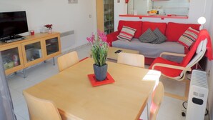 A modern living room with a wooden dining table, red sofa, and a television. - Apartment by Roses Beach With Pool (Roses)