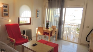 A living room with a red armchair, a wooden table, and a sofa. There is a window with a view of the outside, a radiator, and a door leading to a balcony. - Apartment by Roses Beach With Pool (Roses)