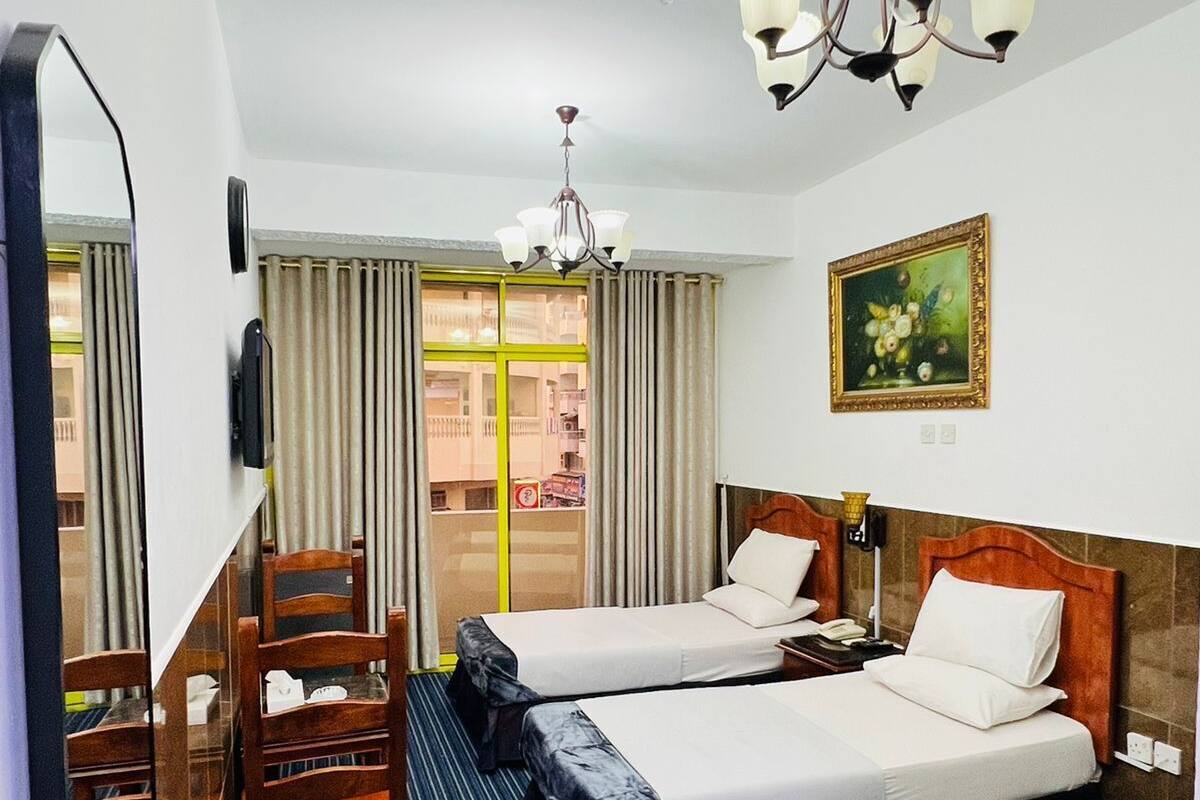 A hotel room with two beds, a large mirror, a chandelier, and a painting on the wall.