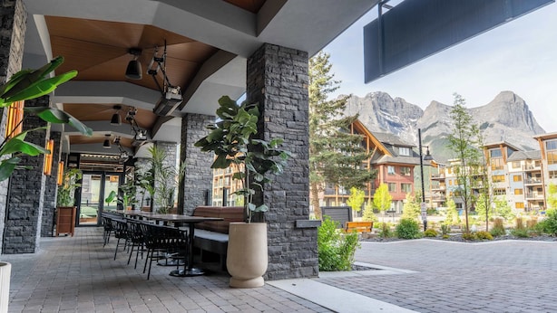 An outdoor patio with a stone wall, wooden ceiling, and potted plants. - Top floor 2 level w hot tub - Modern Mountain Oasis (Canmore)
