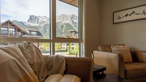 A room with a large window, a leather sofa, a small table, and a framed picture on the wall. - Top floor 2 level w hot tub - Modern Mountain Oasis (Canmore)