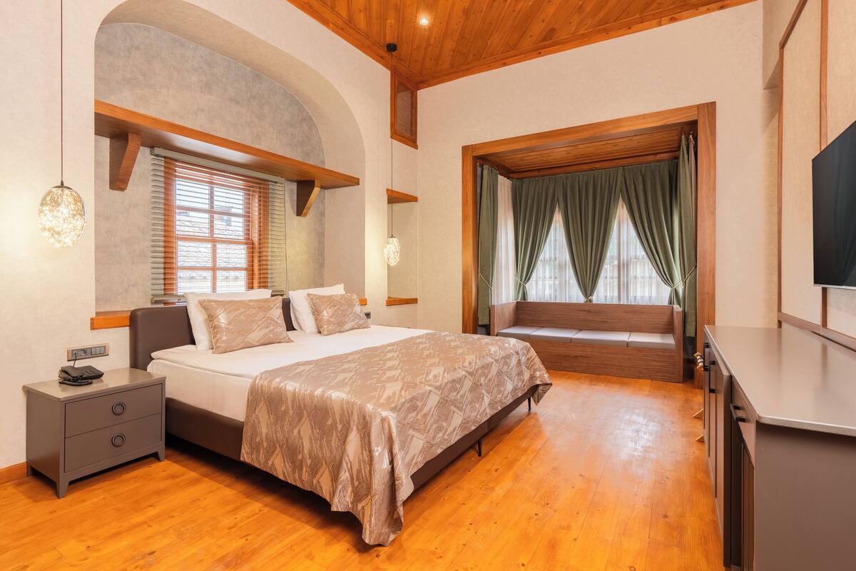 A bedroom with a bed, bedside tables, a TV, and a window with curtains.