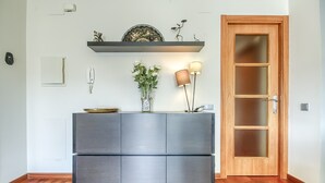 Ein moderner Eingangsbereich mit einer Holztür, einem grauen Konsolentisch mit Dekoration und einem an der Wand befestigten Regal.
