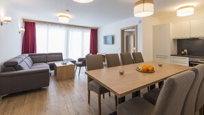 A modern living room with a sofa, dining table, and chairs. There is a kitchen area with cabinets and a countertop. - Apartment in Salzburg With Sunny Terrace (Wagrain)